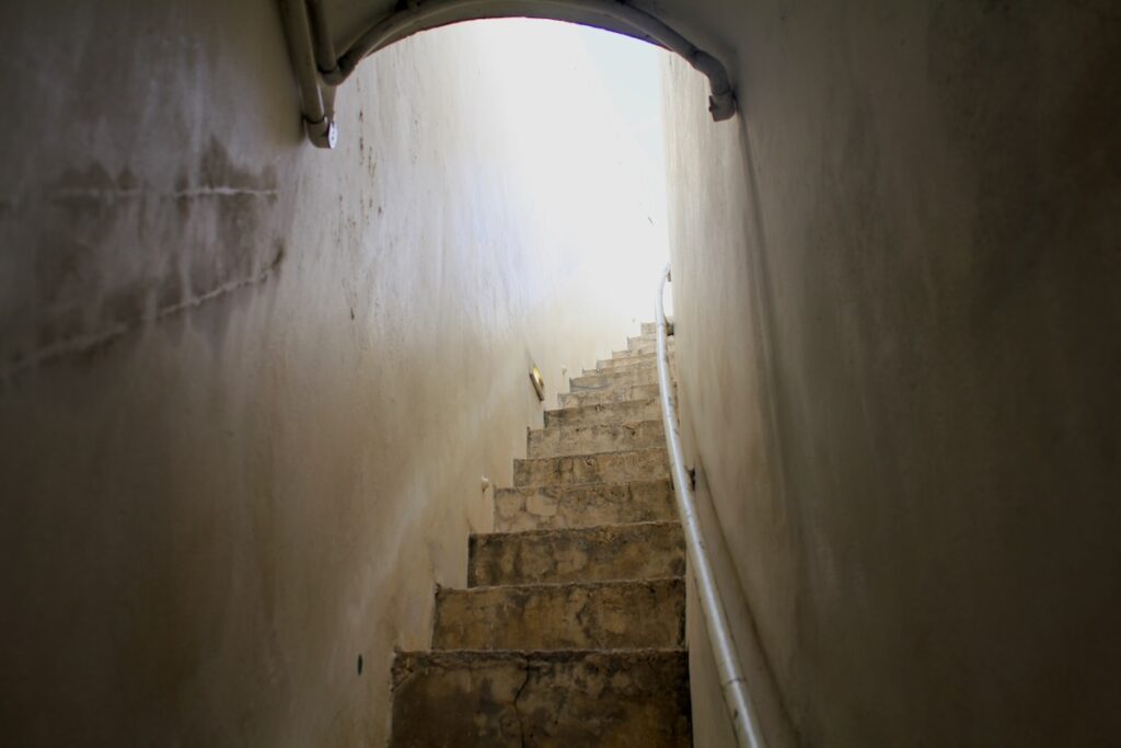 Dimly lit staircase in Wat Prayurawongsawat, Bangkok, with worn concrete steps and aged walls.