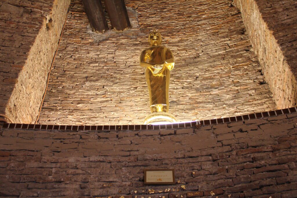 Golden Buddha statue inside a brick chedi at Wat Prayurawongsawat Worawihan, Bangkok, Thailand.