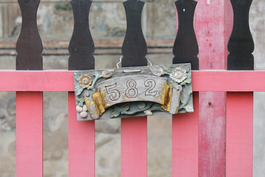 A close-up of a handmade wooden house number sign “582” on a pink fence.